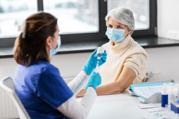 Obraz premium medicine, health and vaccination concept - doctor or nurse filling syringe with vaccine or drug and senior woman in mask at hospital