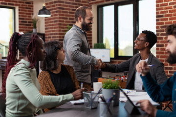 Entrepreneur shaking hand with freelancer during business meeting in startup office. Multi-ethnic businesspeople discussing company turnover working at marketing strategy brainstorming ideas