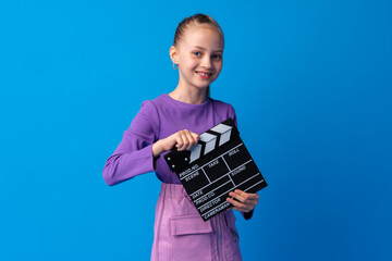 Smiling girl holding clapper board against blue background