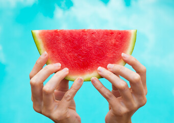 Hand holding slice of watermelon on sky background 