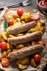 Roast catfish sausages with potatoes, tomatoes and ketchup on a black wooden background. Top view. Copy space