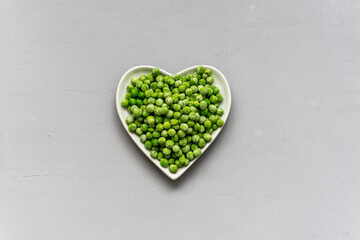 Gefrorene Erbsen auf einem Teller in Herzform auf einem grauen Hintergrund. Draufsicht,...