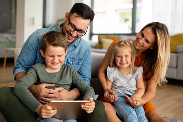 Happy young family having fun time at home. Parents with children using tablet