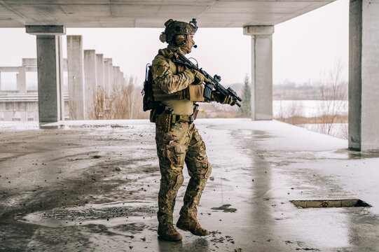 Special forces operator wearing Multicam uniform and his assault rifle HK 416 while practicing CQB combat training in the abandoned building. Coyote brown and mc gear in the urban environment.