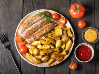 Baked sausages (kupaty), cooked of  catfish, with potatoes, tomatoes with mustard sauce and tomato sauce in a round plate on wooden table in rustic style.