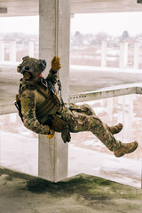 Special forces operator rappeling down the abandoned building on the rope. Multicam camo with coyote brown addons.