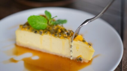 Fork cutting delicious sliced sweet cheesecake decorated with passion fruit jam syrup and fresh mint