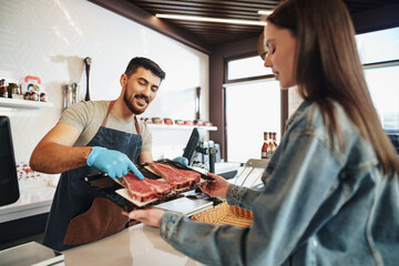 Fototapeta premium Butcher's shop seller helps to choose product to woman customer