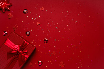 Valentine's Day gift in a red box tied with a red ribbon and red crystals, heart-shaped rubies, rhinestones, glitter on a red background.