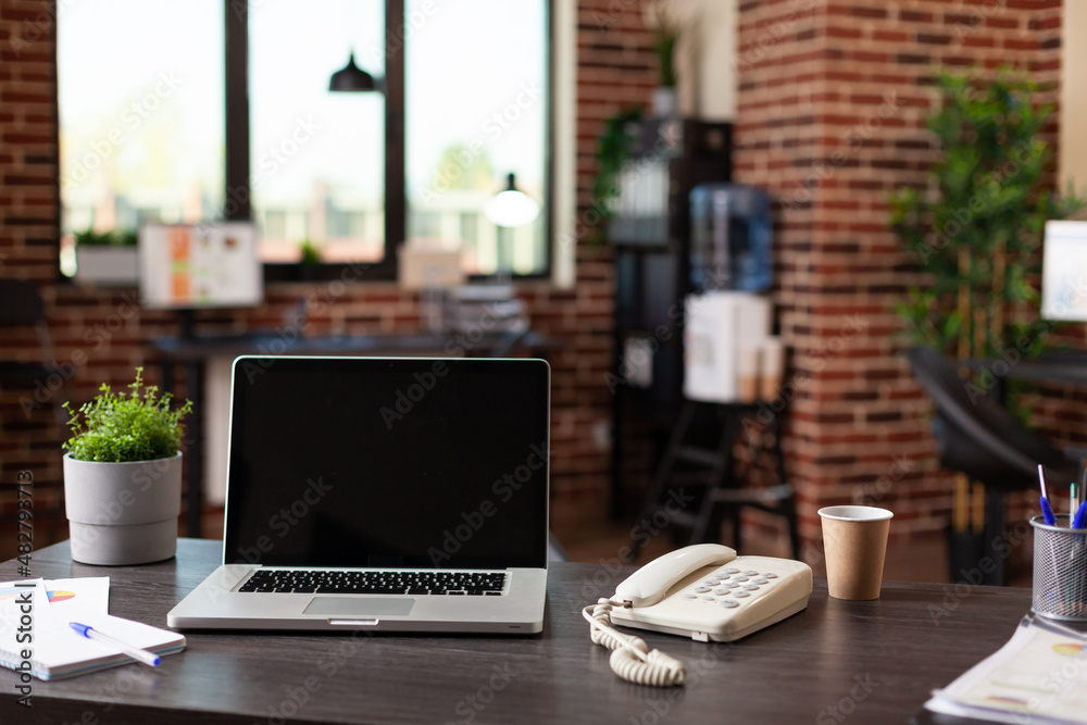 Wall mural Desk with laptop and telephone in empty startup place. Close up of modern computer, landline phone, cup of coffee and office supplies in business workplace. Workspace decor on table