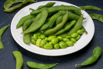 Green Edamame in white plate on wooden background, Steamed edamame sprinkled with sea salt on rustic black wooden table.