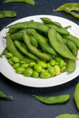 Green Edamame in white plate on wooden background, Steamed edamame sprinkled with sea salt on rustic black wooden table.