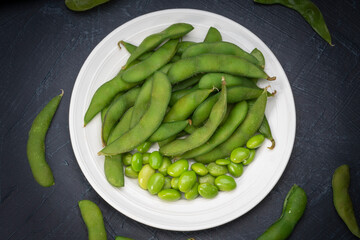 Green Edamame in white plate on wooden background, Steamed edamame sprinkled with sea salt on rustic black wooden table.