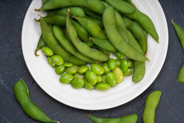 Green Edamame in white plate on wooden background, Steamed edamame sprinkled with sea salt on rustic black wooden table.