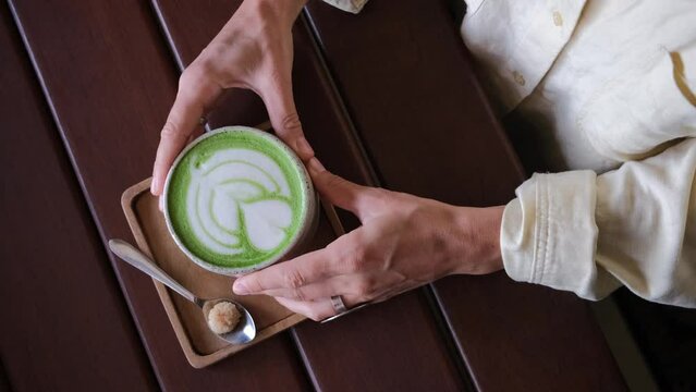 Top view of woman holding in hands trendy green matcha drink with amazing latte art in the hipster cafe 