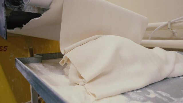 Close-up of piece of dough on the bakery dough rolling machine. Slow motion