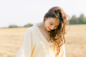 Caucasian young brunette walking through a wheat field. girl in yellow summer dress and straw hat. sheared golden ears of wheat, rye. Close-up portrait of a beautiful girl with brown eyes. 