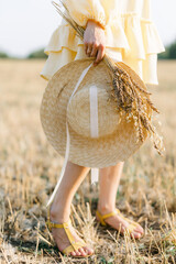 Bare legs of a young girl on a summer day. girl in a yellow dress. Large straw hat with a bouquet of wheat. Agricultural texture