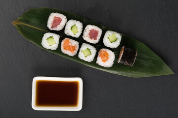 assorted rolls lie on a bamboo leaf next to soy sauce, top view