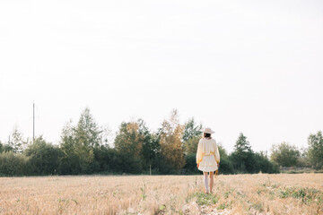 Obraz premium Young beautiful brunette on a summer day. girl in yellow dress. Large straw hat with a bouquet of wheat. Agricultural texture