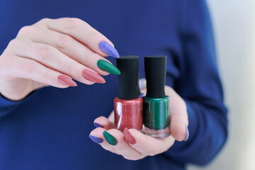 Woman's hands with long nails and multi-colored manicure, bottles of nail polishes