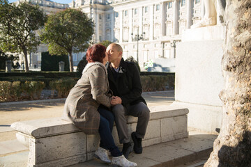 couple woman and senior caucasian man sitting in a park kissing