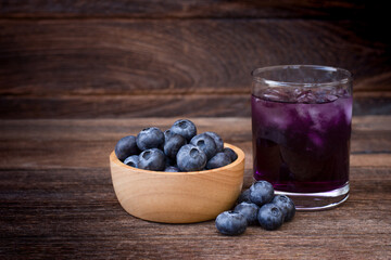 Fresh blueberries fruit in wooden bowl and glass of blueberry juice isolated on wooden table background.