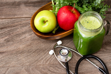 Fresh organic green juice with vegetable and apple with medical stethoscope on wooden table background. Copy space.
