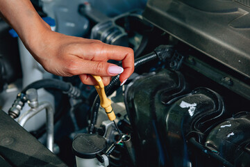 girl's experienced hands are checking an oil in her broken car via an oil dipstick, close up