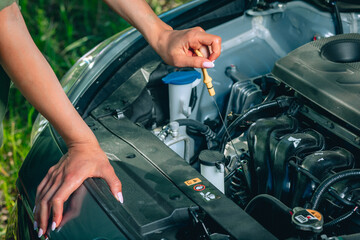lady's soft hands are fixing an oil in her broken car via oil dipstick, close up