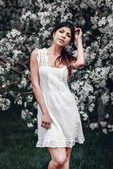 lovely girl in a white dress posing next to a lilac tree on a sunny summer day, portrait