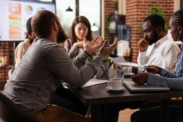 Multi-ethnic businessteam developing marketing project discussing company strategy during business meeting in startup office. Entrepreneurs analyzing financial graph, brainstorming ideas
