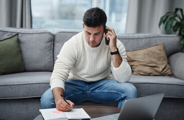 Part living space, part work space. Shot of a young man using a laptop and smartphone while writing in a notebook at home.