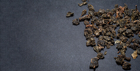 Dry tea with green leaves in wooden spoons, on black background.