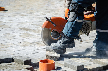 A worker cuts paving slabs with a gas cutter and a hand saw