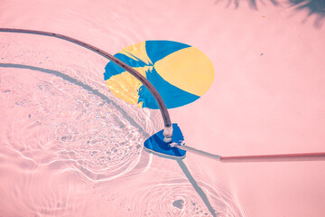 A pink-toned photograph of a pool cleaner using a special vacuum cleaner. Cleaning tools.