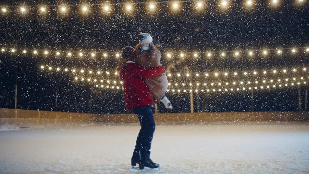 Romantic Winter Snowy Evening: Ice Skating Couple Having Fun on Ice Rink. Pair Skating Boyfrined Lifts His Beautiful Girlfriend and Spins. Love, Dance, Embrace, Figure Skate. Wide Slow Motion