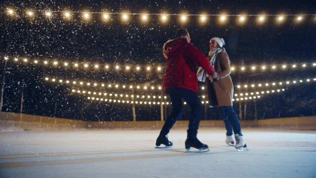 Romantic Winter Snowy Evening: Ice Skating Couple Having Fun on Ice Rink. Pair Figure Skating. Boyfrined Meeting Girlfriend, Starts Dancing. Tender Young People in Love. Wide Shot