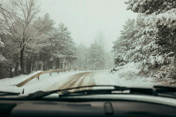 View from inside classic car while driving through snowy highway. Driving in classic car in winter forest countryside.