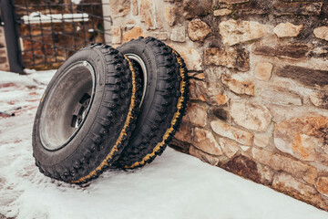 Changing car wheel on a classic car before a race. Studded tyres from old automobile leaning on a stone wall at snowy winter.