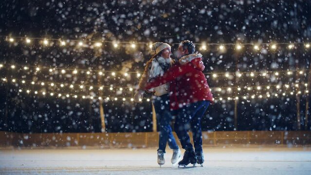 Romantic Winter Snowy Evening: Ice Skating Couple Having Fun, Step on Ice Rink and Start Dancing, waltzing. Pair Figure Skating. Tender Young People, Boyfriend and Girlfriend in Love. Wide Shot