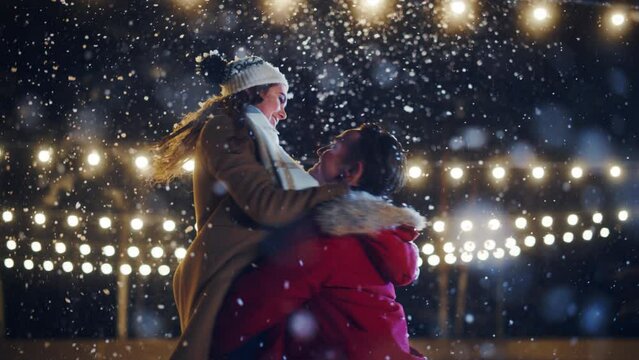 Romantic Winter Snowy Evening: Ice Skating Couple Meeton on Ice Rink and Have Fun. Pair Skating Boyfrined Lifts His Beautiful Girlfriend and Spins. Love, Dance, Embrace, Figure Skate. Wide Slow Motion