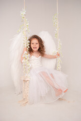a 5-year-old girl rides a swing in an angel costume in a beautiful white dress and wings for Valentine's Day February 14 in love