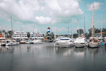 Fototapeta na wymiar Luxury yachts and private boats moored at pier in the seaport. In bacgroung the light cloudy sky