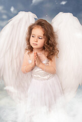 charming little angel girl with huge wings folding her hands to pray against the sky on Valentine's...