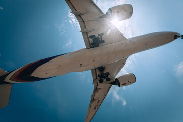 Silhouette of a passenger huge airplane is flying above the blue cloudy sky. View from below.