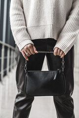 Trendy young girl in a warm cozy sweater shows off a stylish black leather bag.