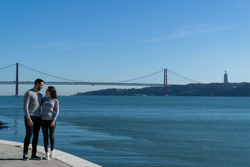 young couple with the 25 april bridge in the background, lisbon, portugal