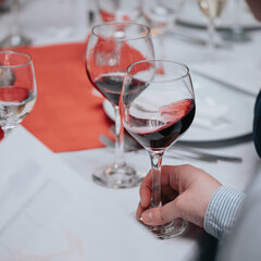 Glass of red wine in hand at a special event, a specific tasting of alcoholic beverages.