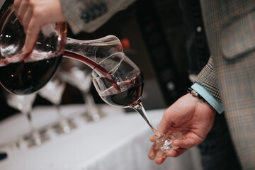 Glass of red wine in hand at a special event, a specific tasting of alcoholic beverages. - 482810502